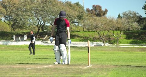 Cricket players competing outdoors with umpire observing gameplay