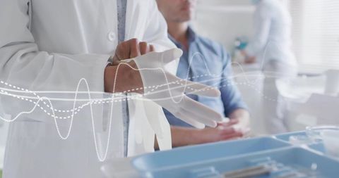 Female doctor donning gloves before patient exam in clinic with blue instrument tray