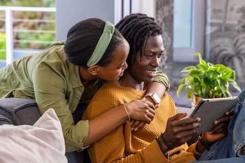 African american couple cuddling on couch while browsing tablet, relaxed cozy home moment