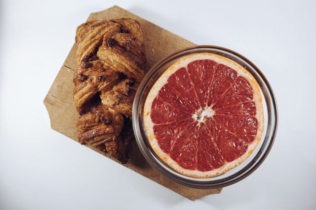 Close-up of halved grapefruit next to flaky pastry on wooden board. Perfect for illustrating healthy breakfast options, nutrition themes or rustic food presentations. Suitable for use in food blogs, advertisements, and cooking magazines.
