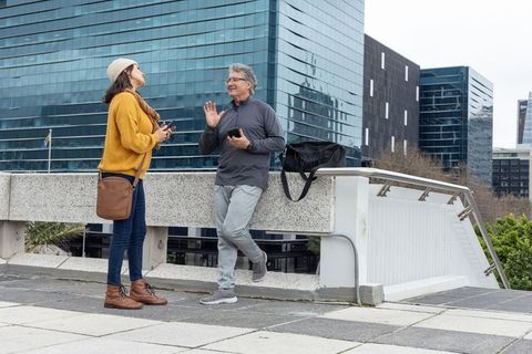 Urban coworkers chatting on office terrace while checking smartphones with duffel bag