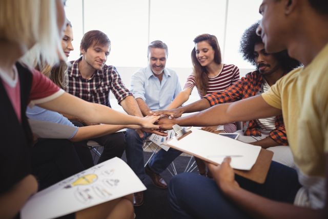 Diverse group of business professionals stacking hands in office meeting, symbolizing unity and teamwork. Ideal for illustrating concepts of collaboration, corporate culture, and team spirit in business presentations, websites, and promotional materials.