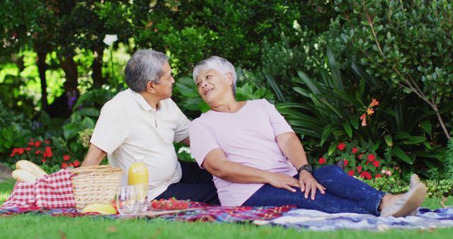 Image of happy biracial senior couple kissing and having picnic in garden. active retirement lifestyle, senior relationship and spending time together concept.