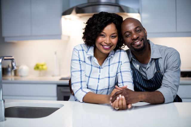 An affectionate couple smiling and embracing each other in a contemporary kitchen. Perfect for advertisements, blog posts, or articles about home life, relationships, and modern living environments.
