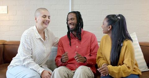 Diverse friends laughing together on brown leather couch during casual home gathering