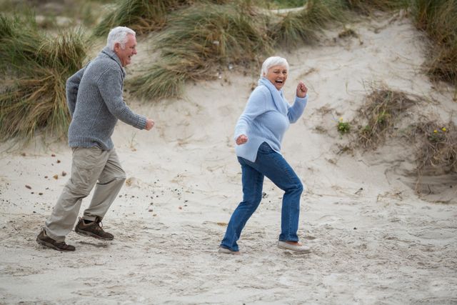 Senior couple enjoying a playful moment at the beach. Ideal for use in advertisements promoting active lifestyles, retirement communities, travel agencies, and health and wellness products aimed at seniors. Perfect for illustrating concepts of happiness, togetherness, and enjoying life in later years.
