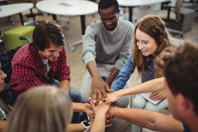 This image shows a diverse group of business executives in an office environment, celebrating unity and teamwork by stacking their hands together. Ideal for illustrating concepts of collaboration, diversity, workplace harmony, and team spirit in business presentations, corporate websites, and motivational materials.