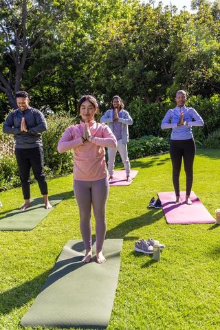 Diverse group practicing yoga outdoors on sunlit lawn for wellness and mindfulness