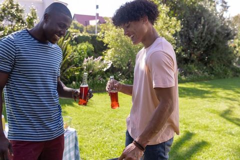 Friends Grilling and Laughing in Sunny Backyard Holding Bottled Drinks
