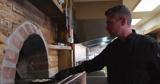Chef handling pizza cooking in a brick oven at a rustic restaurant. Useful for content related to culinary arts, wood-fired pizza preparation, restaurant ambiance, and professional chefs at work. Perfect for food competitions, gastronomic blogs, and cooking tutorials.
