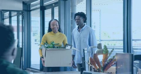 Young professionals moving into modern office carrying box with plant during onboarding
