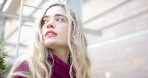 Blonde woman gazing upward under glass canopy urban portrait maroon turtleneck