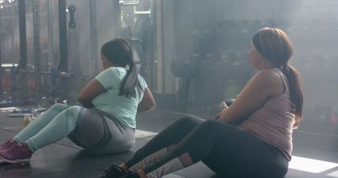 Diverse women performing seated core workout with medicine ball in urban gym studio