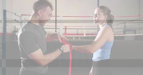 Trainer wrapping boxer hands with red wrap in ring wearing smartwatch and tank top