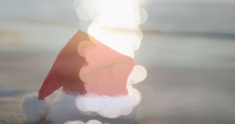 Festive scene features a Santa hat placed on a sunny beach with bright reflections. Perfect for embodying a tropical Christmas vacation theme or celebrating holidays in a seaside location. Useful for travel-related promotions, Christmas event invites, or enhancing a holiday blog with a tropical theme.