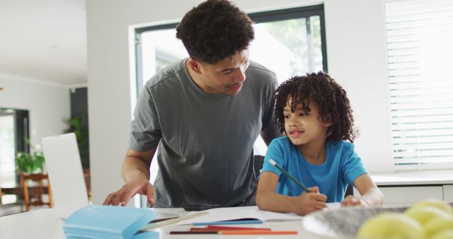 Father and son spending time together. The child doing homework while the adult assisting with work. Useful for concepts of parenting, family bonding, education, home learning, and positive mentor relationship.