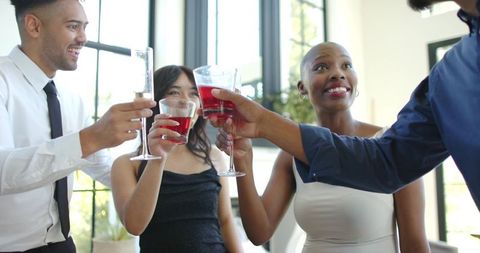 Sunlit modern toasting scene with friends clinking red wine glasses in semiformal attire