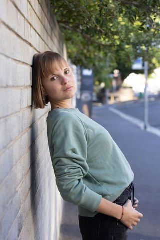 Woman leaning against brick wall on city sidewalk wearing green sweatshirt with nose ring