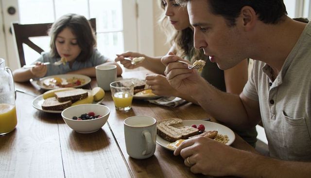 Family enjoying cozy morning breakfast around wooden table with fresh fruit orange juice toast