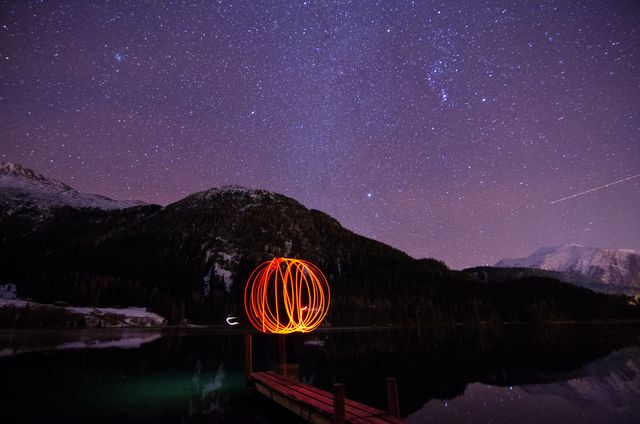 This evocative scene captures a starry night sky with a stunning light painting on a dock over a mountain lake. Ideal for promoting astrophotography, nighttime serenity, nature retreats, outdoor adventure magazines, or travel brochures emphasizing tranquil and scenic outdoors. Can be used to highlight the beauty of natural landscapes and the allure of the cosmos.
