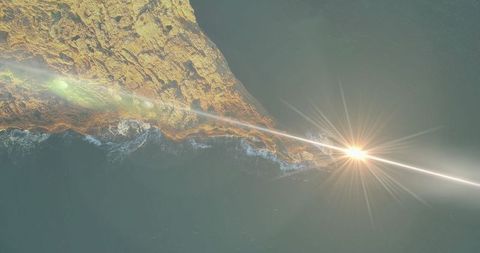 Aerial View of Rocky Coastline with Sunburst Over Ocean at Sundown