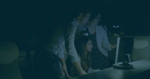 Colleagues collaborating late night around computer screen under desk lamp for team project