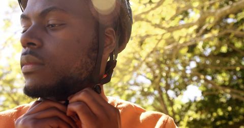 a young man adjusting his headphones outdoors with a thoughtful expression, suggesting preparation for enjoying music or a podcast. sun filtering through trees adds warmth, making it ideal for lifestyle blogs, audio teams, or advertisements focused on outdoor leisure and relaxation.