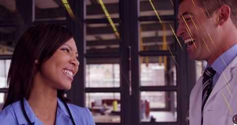 Smiling nurse and doctor collaborating and laughing in modern clinical corridor
