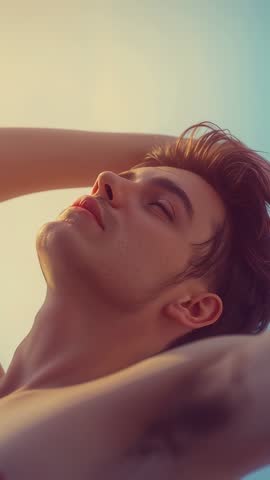 Reclining shirtless man posing with arms behind head in soft-gradient studio vertical video