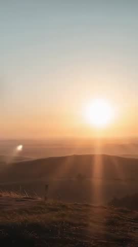 Vertical sunrise over moorland crest with golden rays, lens flare and silhouetted signpost