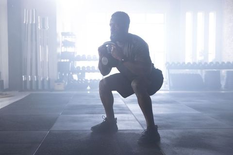 African american athlete performing kettlebell goblet squat in light-filled gym strength training