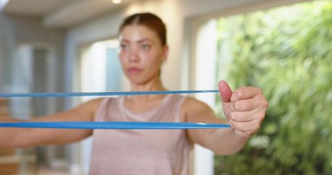 Woman pulling blue resistance band for home strength training, rehab and arm toning