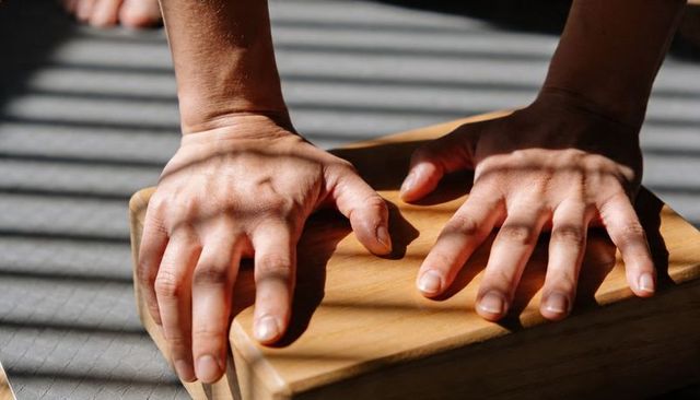Pressing hands on wooden yoga block casting striped blind shadows in morning light