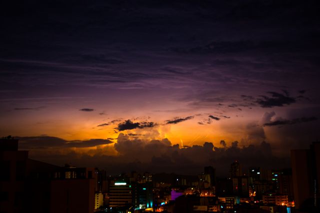City skyline with buildings illuminated by dramatic night sky featuring lightning. Suitable for use in promotional materials, cityscape photography collections, and weather-related content. Great for blogs, websites, and articles discussing urban life, weather events, and twilight scenery.