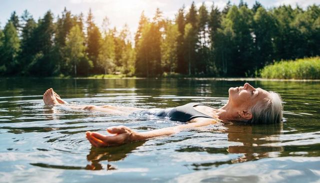 Senior woman floating peacefully on calm lake at golden hour, relaxing in tranquil nature