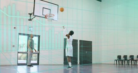 Male basketball player shooting jump shot during indoor practice with coach observing