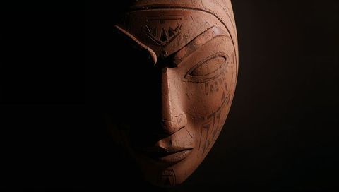 Dramatic carved wooden mask with tribal engravings and warm gallery lighting
