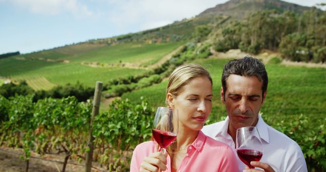 A middle-aged Caucasian couple enjoys a wine tasting experience in a picturesque vineyard, with copy space. Their relaxed demeanor and the scenic backdrop suggest a leisurely getaway or a romantic retreat.