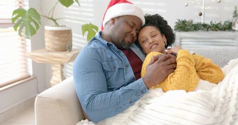 Couple cuddling on sofa under blanket cozy holiday morning with santa hat and sunlight