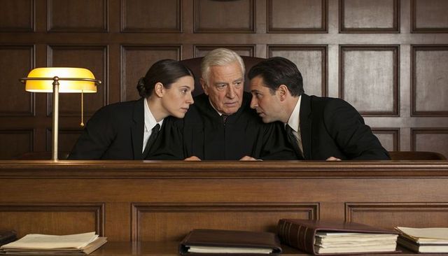Judge conferring with male and female lawyers behind wood bench in classic courtroom