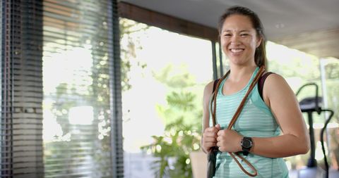 Active Asian Woman Embracing Skipping Rope in Bright Home Gym