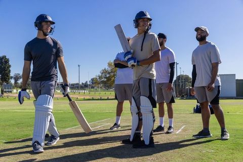Cricket teammates preparing for batting practice on sunny grass pitch