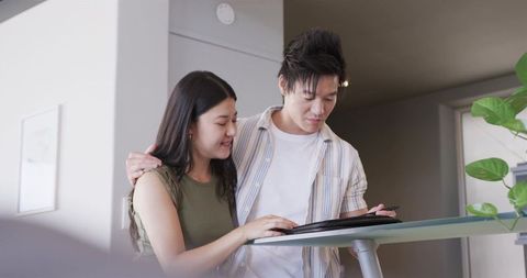 Young asian couple using tablet and stylus in modern minimalist apartment