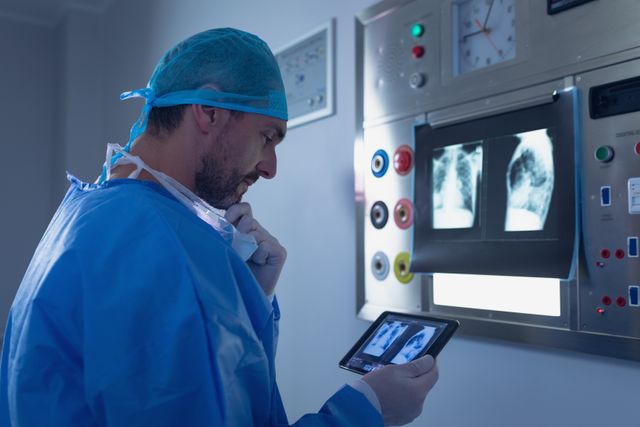 Male surgeon examining x-ray report on digital tablet in operating room at hospital