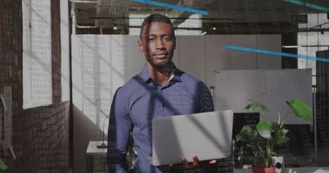 Confident developer standing with laptop in industrial office with code reflection