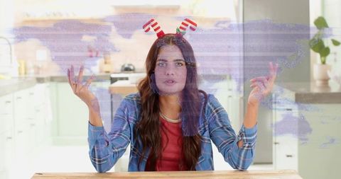 Woman wearing candy cane antler headband talking at kitchen table with purple glitch overlay