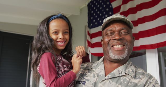 Delightful scene of a military father holding his young daughter in front of American flag. Perfect for themes of family, patriotism, military life, and father-daughter relationships. Can be used for community, veterans, or family-oriented projects.