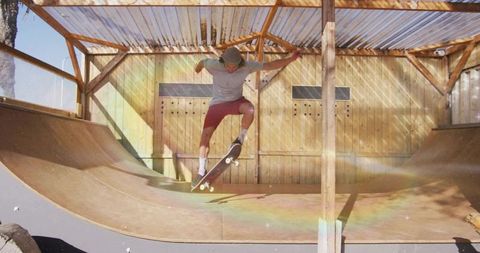 Skateboarder performing trick on wooden backyard half-pipe ramp with lens flare
