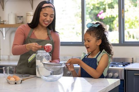 Mother and daughter baking together, sifting flour on sunlit marble kitchen countertop