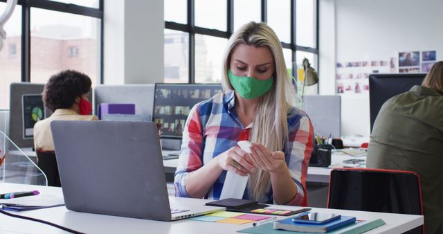 Businesswoman Wearing Green Face Mask Disinfecting Desk in Modern Office - Download Free Stock Images Pikwizard.com